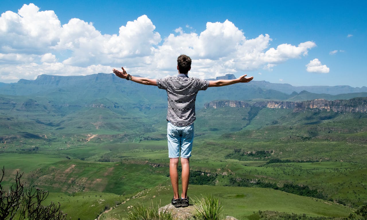 Home A man stands triumphantly with arms open, overlooking a scenic mountain range.